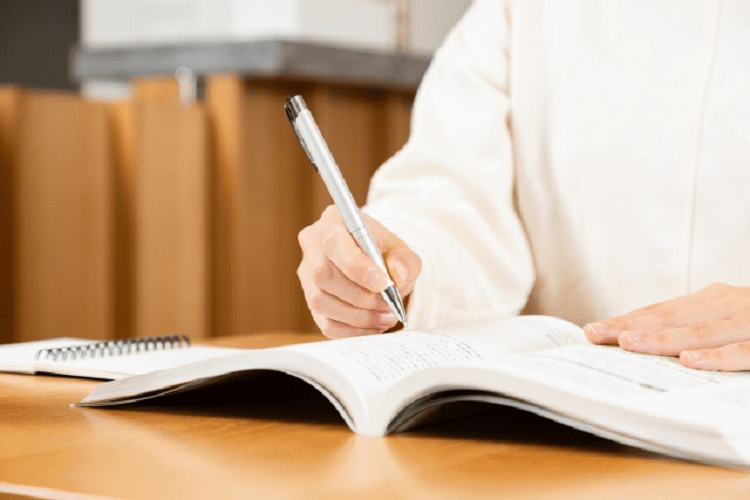 ペンを持つ人の手と参考書