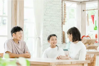 明るいリビングで父親、母親、子供の3人家族がテーブルを囲んで資料を見ながら和やかに話し合っている様子の写真