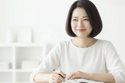 白い服を着て机でノートに書き込む女性